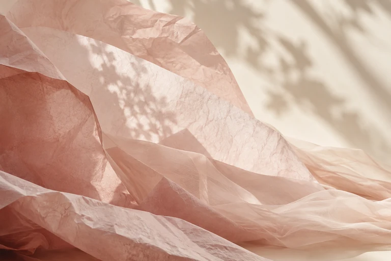 Sculptural folds of soft pink paper in warm light